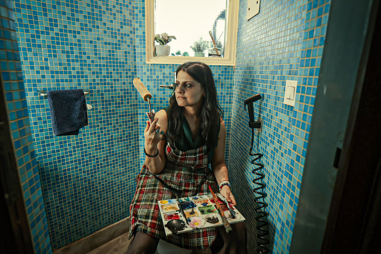 Shivani Garg holding a paint roller beside a palette against blue mosaic tiles