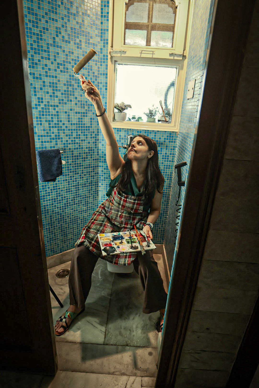 Shivani Garg reaching up with a paint roller in her turquoise-tiled studio room