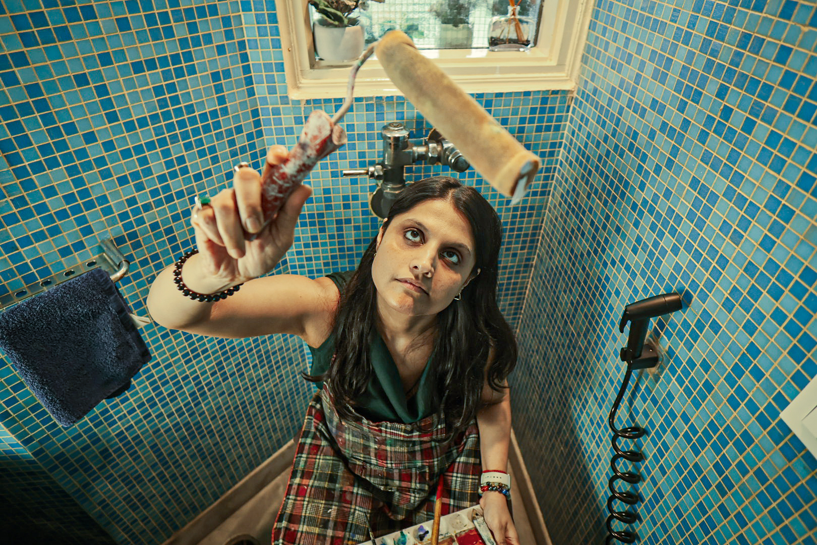 Shivani Garg holding a paint roller above her head in the turquoise-tiled room, seen from below