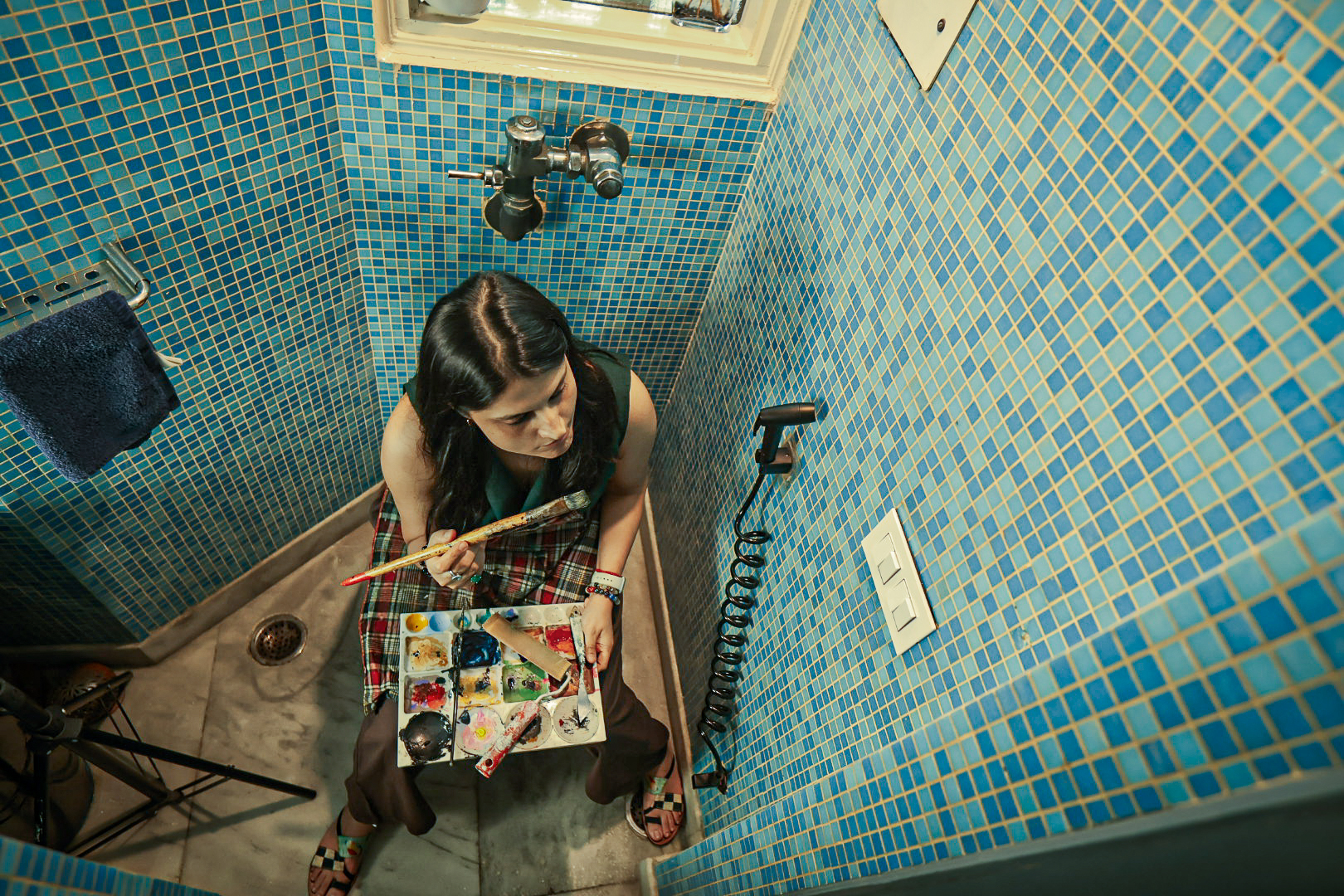 Shivani Garg seen from above, seated with a palette and brush against blue mosaic tiles