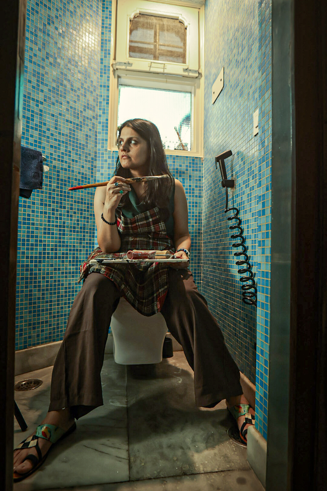 Shivani Garg seated with a brush raised, palette on her lap, in the turquoise-tiled room