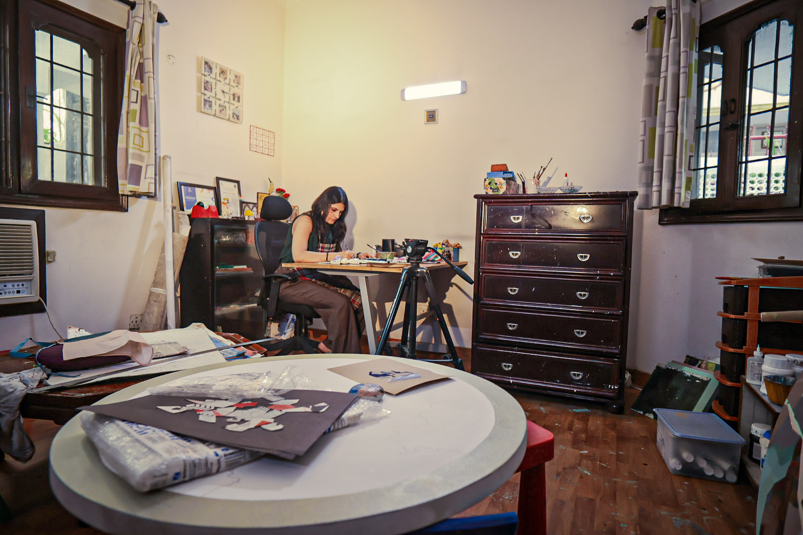 A wide view of the studio room with the artist at her desk and a round table in the foreground