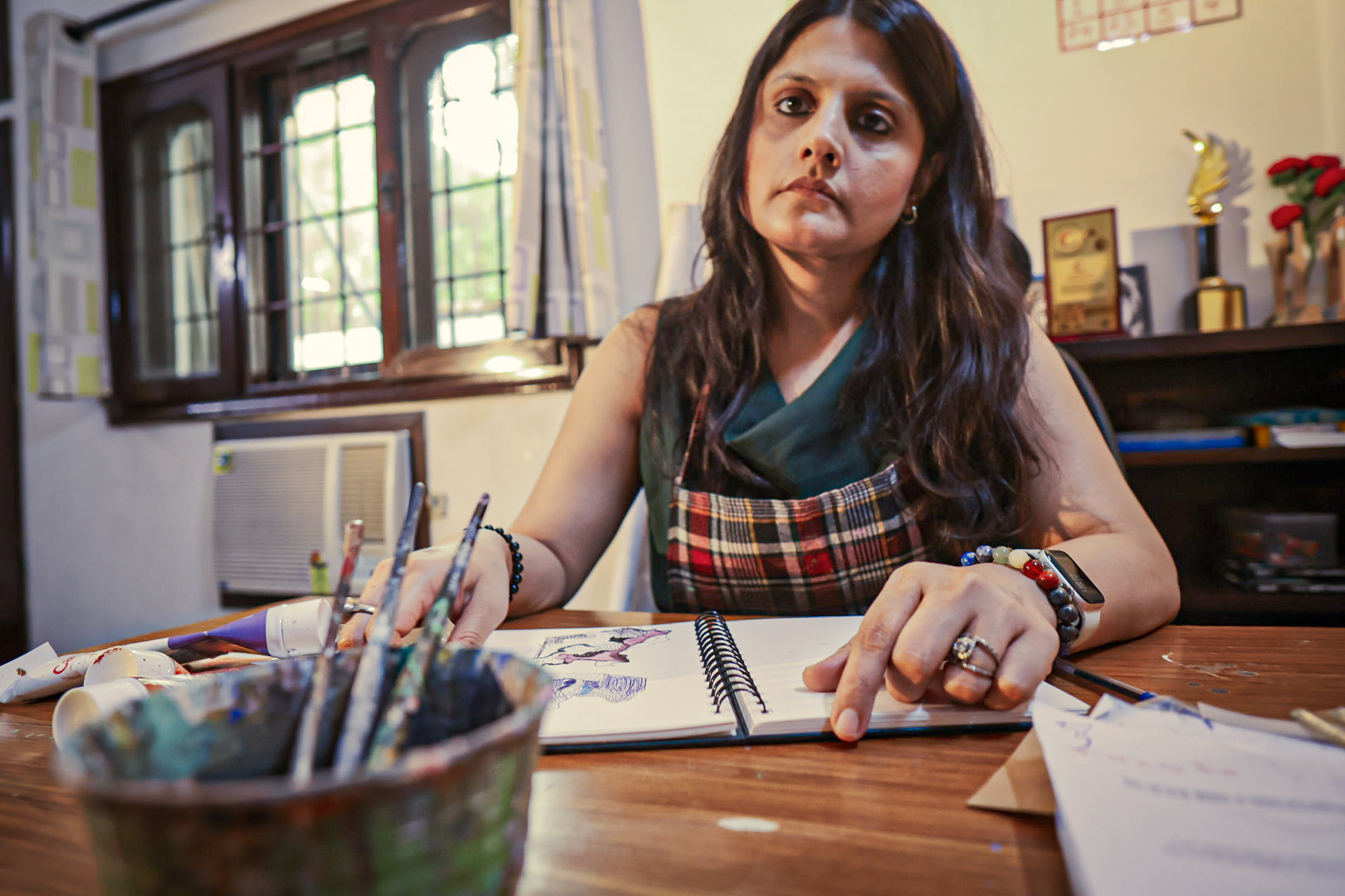 Shivani Garg at her desk with a sketchbook and brushes