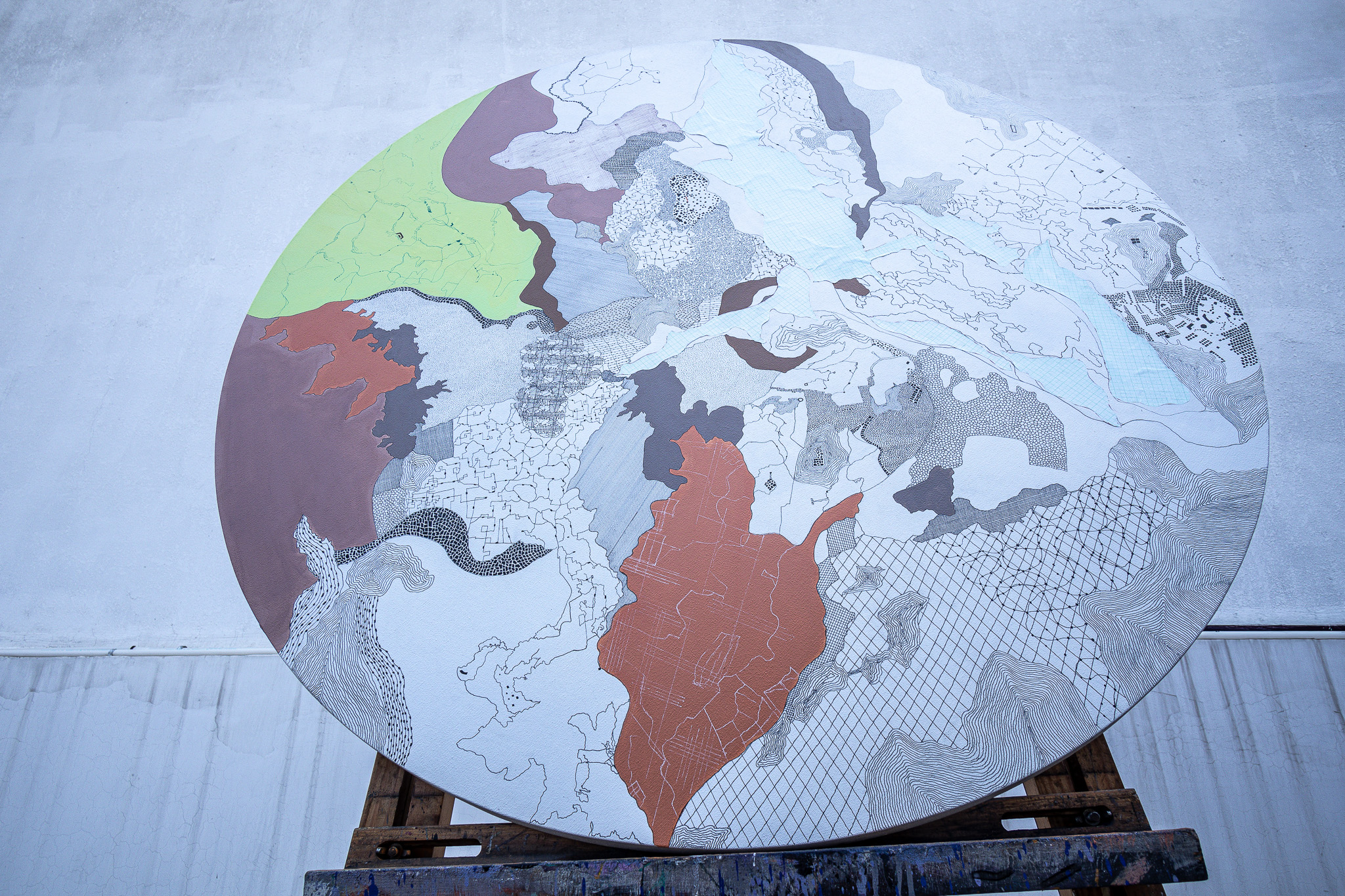 Circular artwork with pale map-like fragments and green and rust-coloured areas